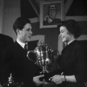 Motorcycle racing champion Geoff Duke shows the trophy to film star Joan Rice