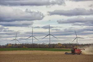 A Combine Harvests Soybeans While Wind Turbines Spin In The Distance; Strathroy, Ontario, Canada A Combine Harvests Soybeans While Wind Turbines Spin In The Distance; Strathroy, Ontario, Canada
