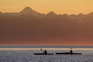 Two Female Sea Kayakers Enjoy A Warm Summer Evening While Paddling In Favorite Passage Two Female Sea Kayakers Enjoy A Warm Summer Evening While Paddling In Favorite Passage