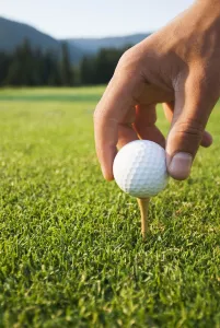 Golfer Sets Up A Ball On The Tee Of A Golf Course On A Summer Evening; Whistler Golfer Sets Up A Ball On The Tee Of A Golf Course On A Summer Evening; Whistler
