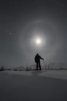 Man Snowshoeing Along The Dempster Highway Under A Moon Glowing With Rings; Yukon, Canada Man Snowshoeing Along The Dempster Highway Under A Moon Glowing With Rings; Yukon, Canada