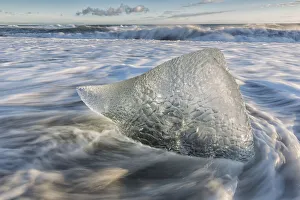 Small Iceberg Surrounded By Flowing Water Along The Southern Coast Of Iceland With Large Waves Crashing Against The Small Iceberg Surrounded By Flowing Water Along The Southern Coast Of Iceland With Large Waves Crashing Against The
