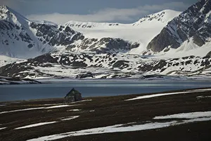Small Wooden Cabin On The Shore Of The Arctic Ocean And Snow Covered Mountains; Spitsbergen, Svalbard, Norway Small Wooden Cabin On The Shore Of The Arctic Ocean And Snow Covered Mountains; Spitsbergen, Svalbard, Norway