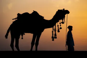 Young boy standing with his decorated camel in the desert of Northern India Young boy standing with his decorated camel in the desert of Northern India