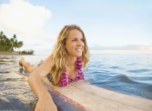A Young Woman Wearing A Lei Rides A Surfboard Out In The Water; Maui, Hawaii, United A Young Woman Wearing A Lei Rides A Surfboard Out In The Water; Maui, Hawaii, United